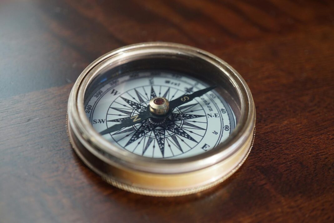 Close-up of a vintage compass resting on a warm, dark wooden surface, indicating navigation and exploration.