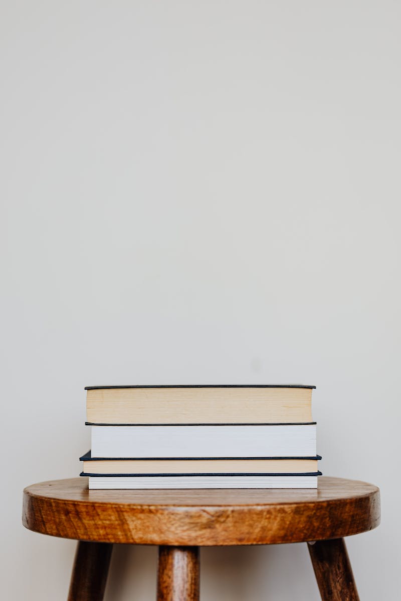 Close-up of three hardcover books stacked on a wooden stool against a plain background.