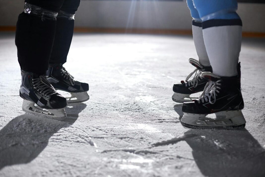 A close-up view of two pairs of ice skates on an ice rink, highlighting the skating gear.