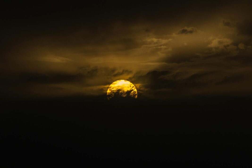 A captivating image of the moon partially covered by dark clouds, creating a dramatic sky at dusk.