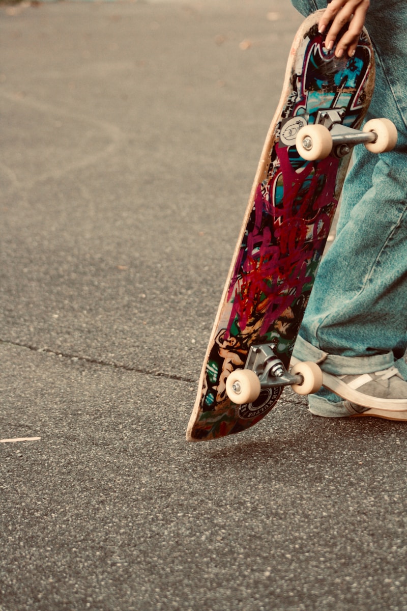 Person holding a graffiti-decorated skateboard on pavement
