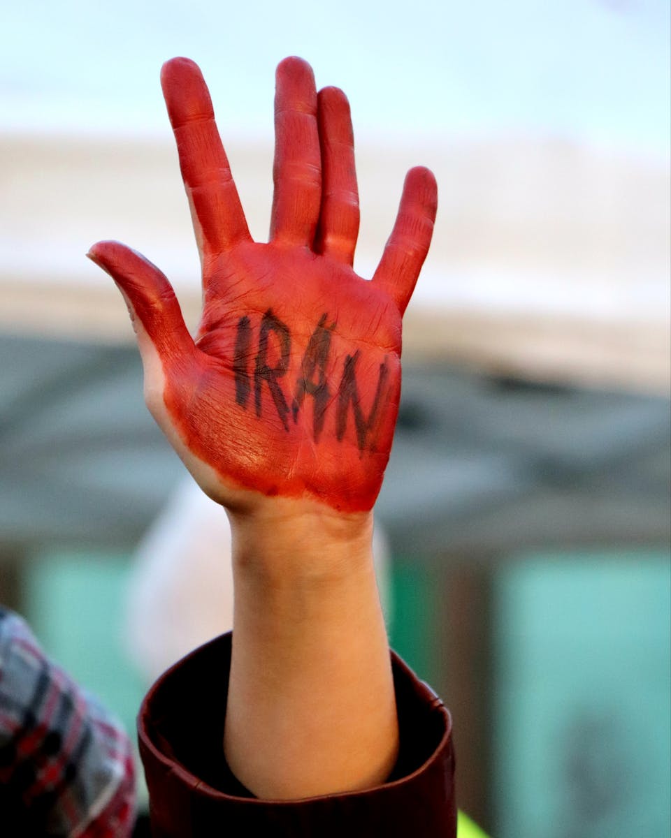 A close-up of a hand painted red with 'Iran' written on it, symbolizing protest.