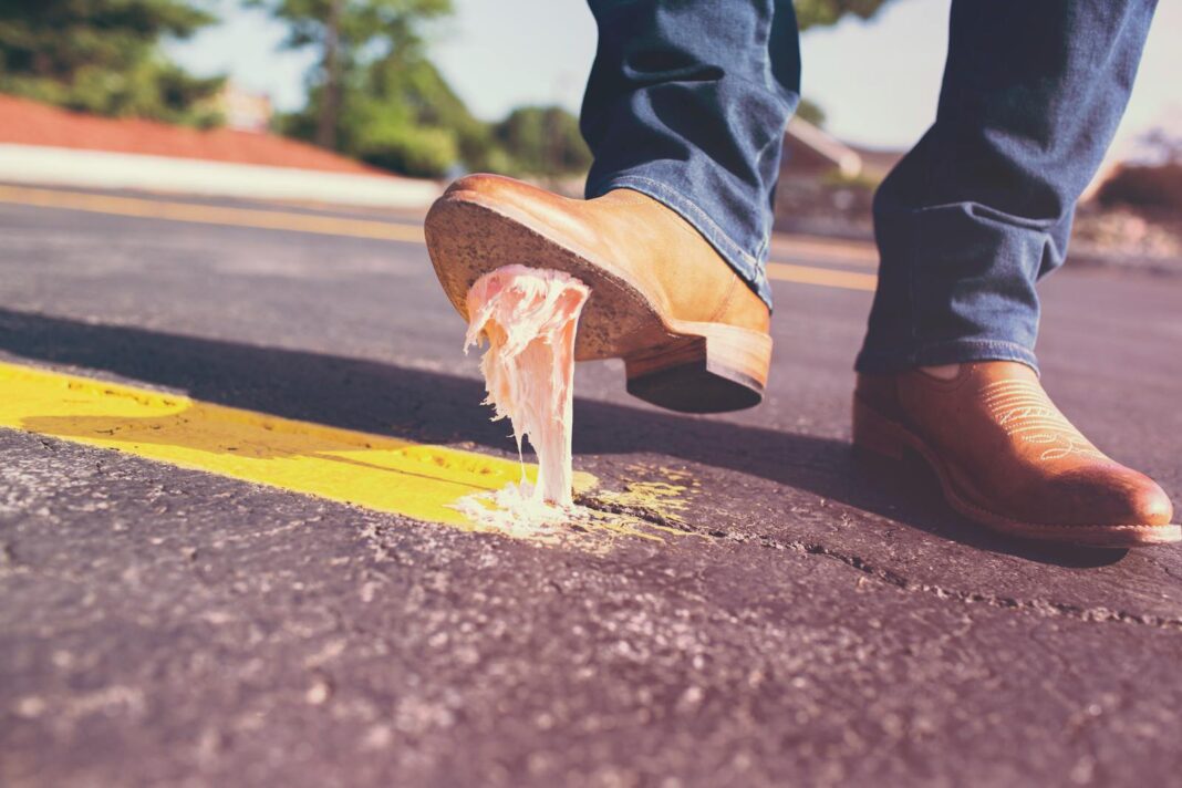 Close-up of a man's shoe getting stuck with chewing gum on the street, illustrating an everyday mishap.