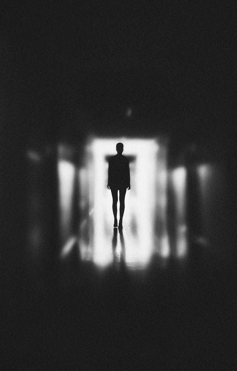 Moody silhouette of a person in a blurred, black and white corridor. Capturing themes of solitude and mystery.