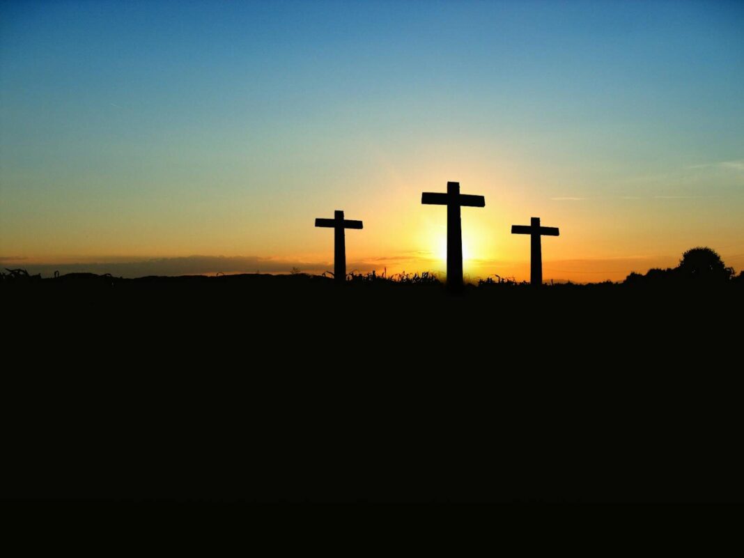 Silhouette of three crosses against a vibrant sunset sky.