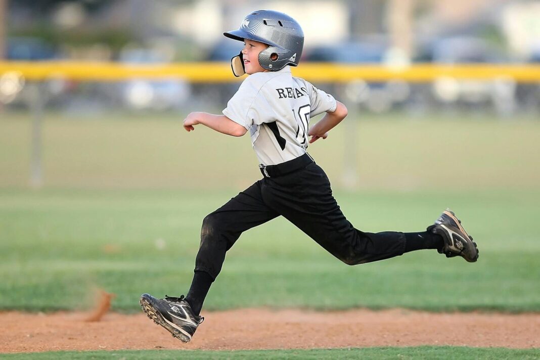 Action shot of a young baseball player running fast on the field, wearing uniform and helmet.