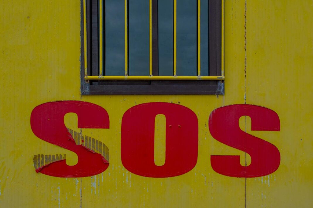 Close-up of SOS sign on a yellow wall with window above, urban setting.