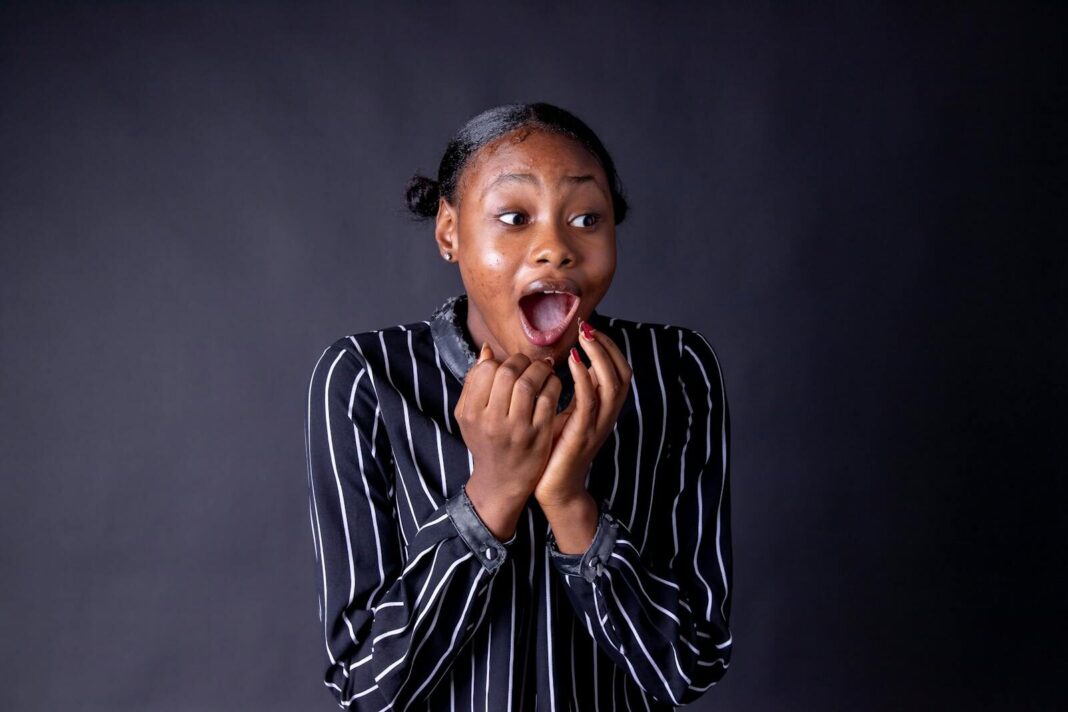 An expressive portrait of a young woman with an amazed expression and striped shirt on a gray background
