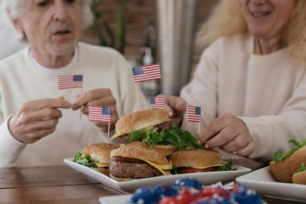 Senior couple enjoying burgers with American flags, embodying patriotic celebration.